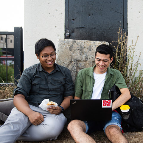 Two male students smiling, looking at laptop