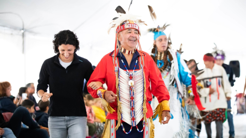 A group of people dancing at the ƻԺ Powwow. Some are wearing colourful regalia