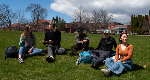 Five students lounge on the grass outside of the Macdonald-Stewart building