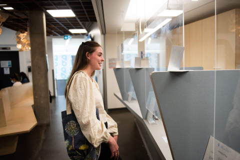 A student standing at the reception counter for the Student Wellness Hub, greeted by a seated staff member