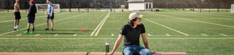 Student sits in front of football field at ƻԺ's Molson stadium.